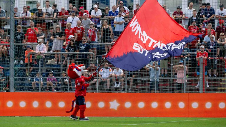 Maskottchen Fonsi lässt die Fahne der SpVgg Unterhaching vor den Fans wehen.