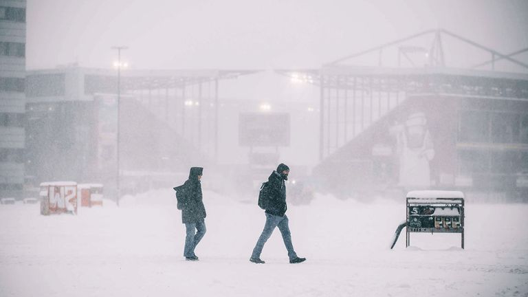 Menschen in Hamburg gehen im Schneegestöber über das Heiligengeistfeld am Millerntor-Stadion vorbei.