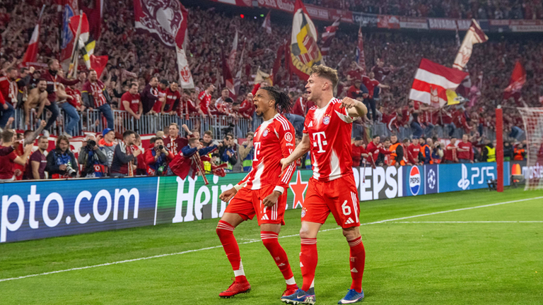 Michael Olise (l.) und Joshua Kimmich (r.) feiern den Sieg vor den Bayern-Fans. Im Halbfinale geht es 28. April gegen PSG. 